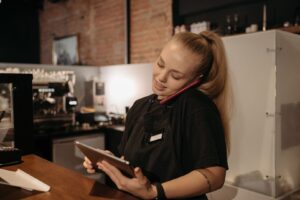 Mitarbeiterin im Café telefoniert und hält ein Tablet am Arbeitsplatz